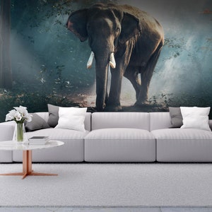 May include: A detailed mural depicting an elephant in a misty forest. The elephant, with its tusks and textured skin, is the focal point. The mural is mounted above a white sectional sofa, with a round coffee table and a vase of white flowers.