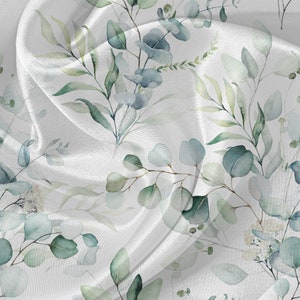May include: White fabric with a watercolor pattern of green leaves and blue flowers. The fabric is draped and flowing.