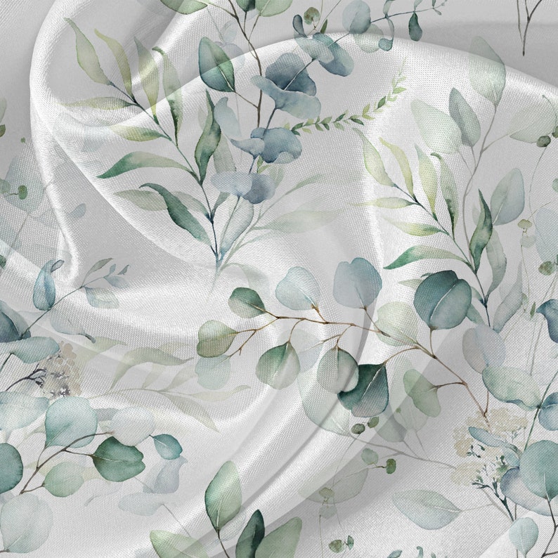 May include: White fabric with a watercolor pattern of green leaves and blue flowers. The fabric is draped and flowing.