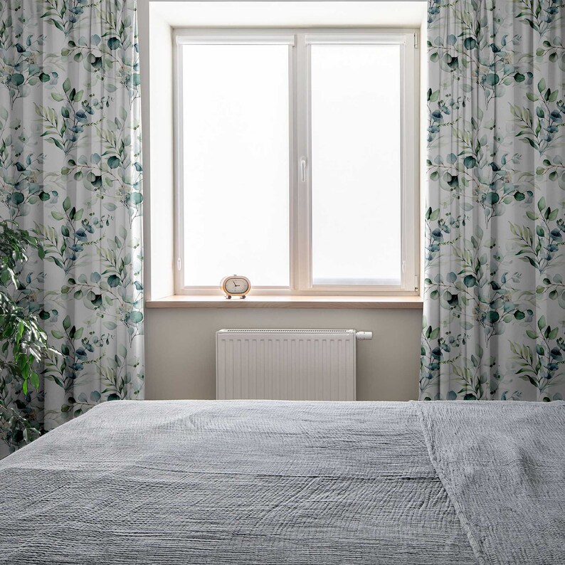 May include: A gray bed with a white radiator and a window with white curtains featuring a green leaf pattern.