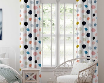 May include: A pair of white curtains with a colorful polka dot pattern. The curtains have grommet tops and are hung on a window with white blinds. A white wicker chair with a white cushion and a gold pillow is in the foreground.