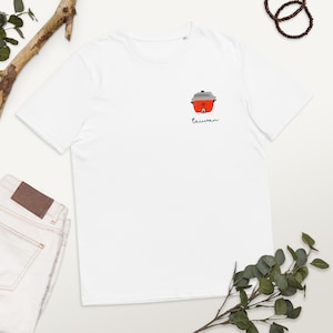 Puede incluir: Camiseta blanca con un pequeño dibujo de una arrocera roja y gris y la palabra "taiwan" debajo. La camiseta se muestra sobre una superficie blanca, junto con unos vaqueros y elementos decorativos.