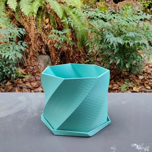 May include: A teal blue geometric planter with a twisted design. The planter has a hexagonal base and a hexagonal top.