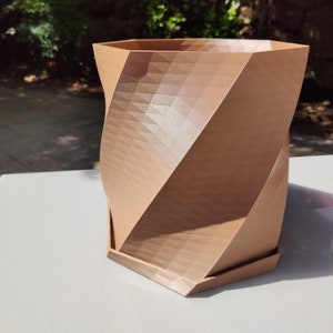 May include: A brown, geometrically shaped planter with a textured surface. The planter has a hexagonal base and a slightly flared top.
