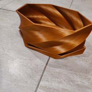 May include: A brown, 3D printed planter with a unique, swirling design. The planter is made of a smooth, textured plastic and has a wide, open top.