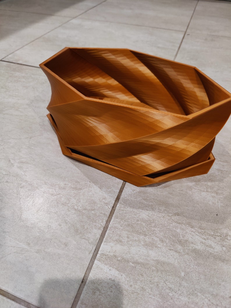 May include: A brown, 3D printed planter with a unique, swirling design. The planter is made of a smooth, textured plastic and has a wide, open top.