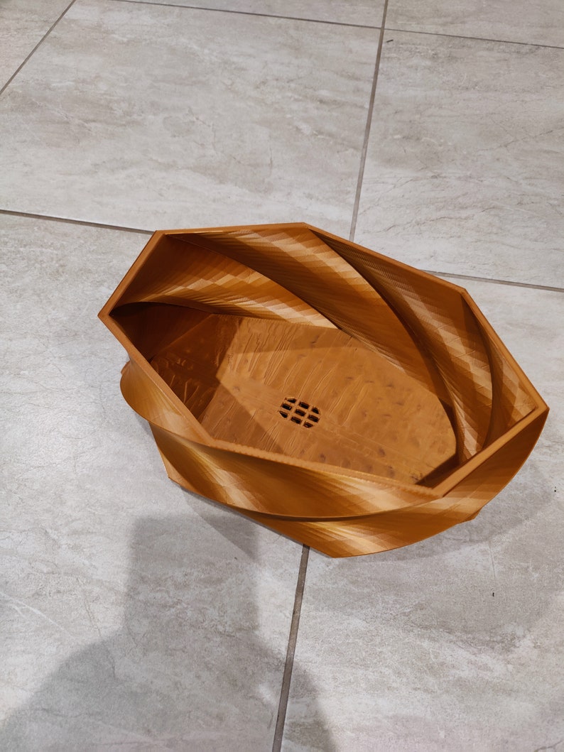 May include: A brown, wooden, geometric planter with a swirl design. The planter has a drainage hole in the bottom.