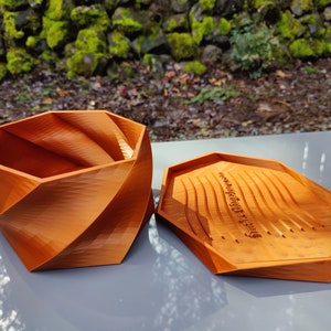 May include: A wooden, orange-brown, geometric box with a lid. The lid has a carved inscription that reads "Never underestimate the power of dreaming".