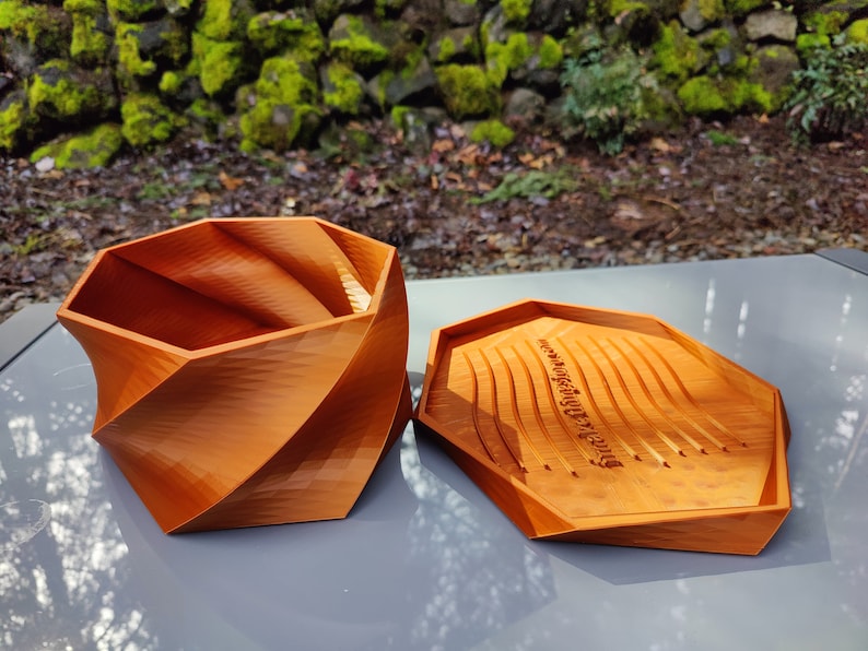 May include: A wooden, orange-brown, geometric box with a lid. The lid has a carved inscription that reads "Never underestimate the power of dreaming".