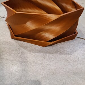 May include: A brown, 3D printed, hexagonal planter with a swirling design. The planter has a separate base.