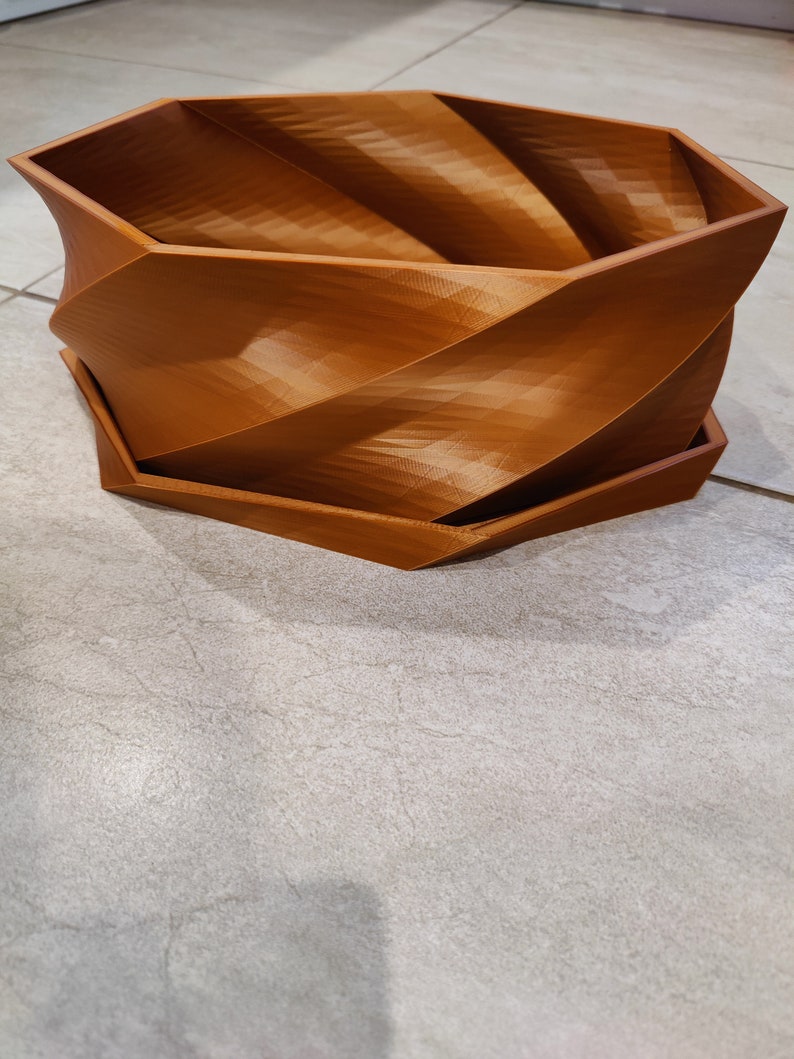 May include: A brown, 3D printed, hexagonal planter with a swirling design. The planter has a separate base.