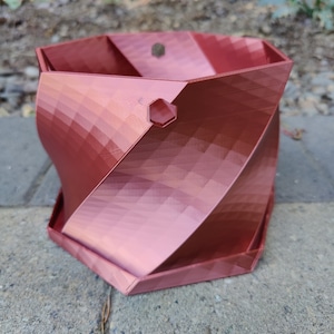 May include: A red, hexagonal, 3D printed planter with a twisted design. The planter has a drainage hole on the side.