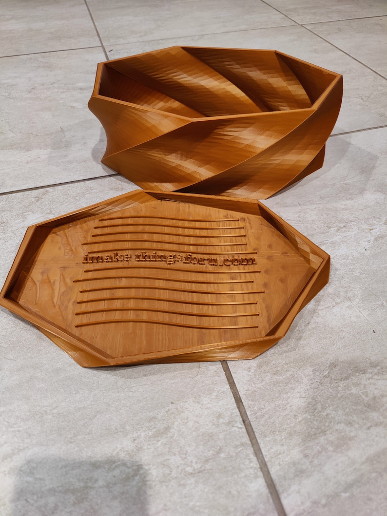 May include: A wooden box with a unique, swirling design. The lid is open and the inside of the box is visible. The box is made of light brown wood and has a natural finish. The box is labeled with the text "make things form.com".