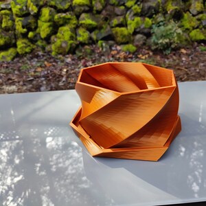 May include: A geometric orange planter with a unique spiral design. The planter is made of a smooth, textured material and has a hexagonal shape.