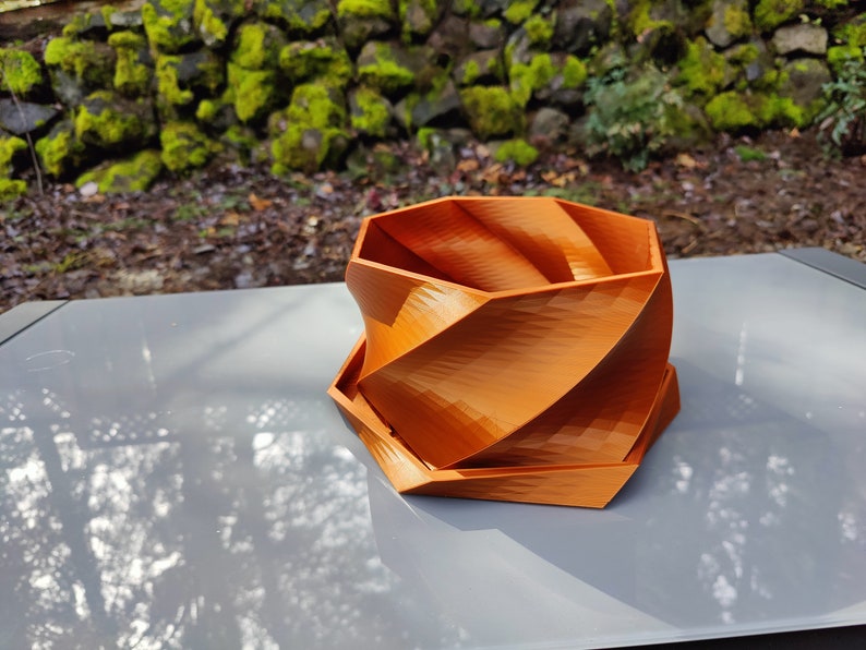 May include: A geometric orange planter with a unique spiral design. The planter is made of a smooth, textured material and has a hexagonal shape.
