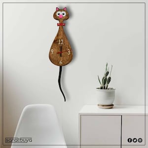 May include: A brown wooden cat-shaped clock with a red bow tie and pink eyes. The clock has black hands and white numbers. The clock is hanging on a white wall.