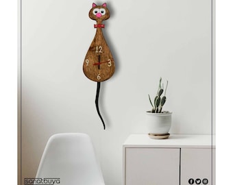 Puede incluir: Un reloj de madera marrón con forma de gato con una corbata de lazo roja y ojos rosas. El reloj tiene agujas negras y números blancos. El reloj está colgado en una pared blanca.
