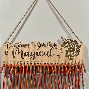 Könnte beinhalten: Holz-Countdown-Kalender mit einem Einhorn-Design und dem Text "Countdown to Something Magical". Der Kalender hat 24 Fächer für Zuckerstangen.