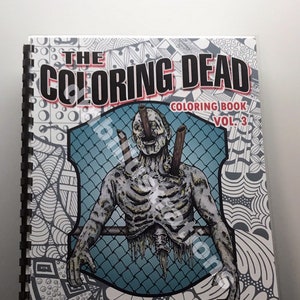May include: The Coloring Dead coloring book, volume 3, features a black and white illustration of a zombie with a skeletal appearance, trapped behind a fence. The book cover has a black and white patterned background.