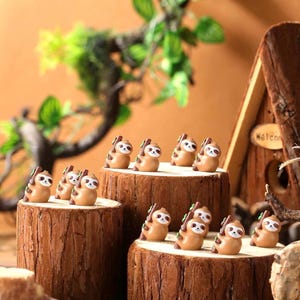 May include: A collection of small, tan-colored sloth figurines, each holding a small branch, arranged on wooden platforms. The sloths have white faces and are set against a backdrop of greenery and a wooden house.