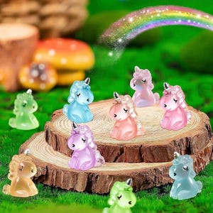 May include: A collection of miniature, colorful unicorn figurines in various pastel hues, including pink, blue, green, and yellow. The unicorns are arranged on a small wooden slice, set against a backdrop of green grass and a whimsical rainbow.