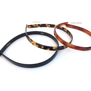 May include: Three plastic headbands in different colours and patterns. The headband at the top is brown with a tortoiseshell pattern and the text "TORTOISE" above it. The headband in the middle is brown with a tortoiseshell pattern and the text "TOKYO" above it. The headband at the bottom is black.