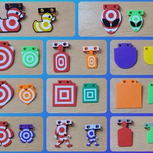 May include: A collection of colorful shooting targets in various shapes, including ducks, aliens, and geometric designs. The targets feature red, white, green, orange, purple, and yellow color schemes. Each target has a mounting bracket.