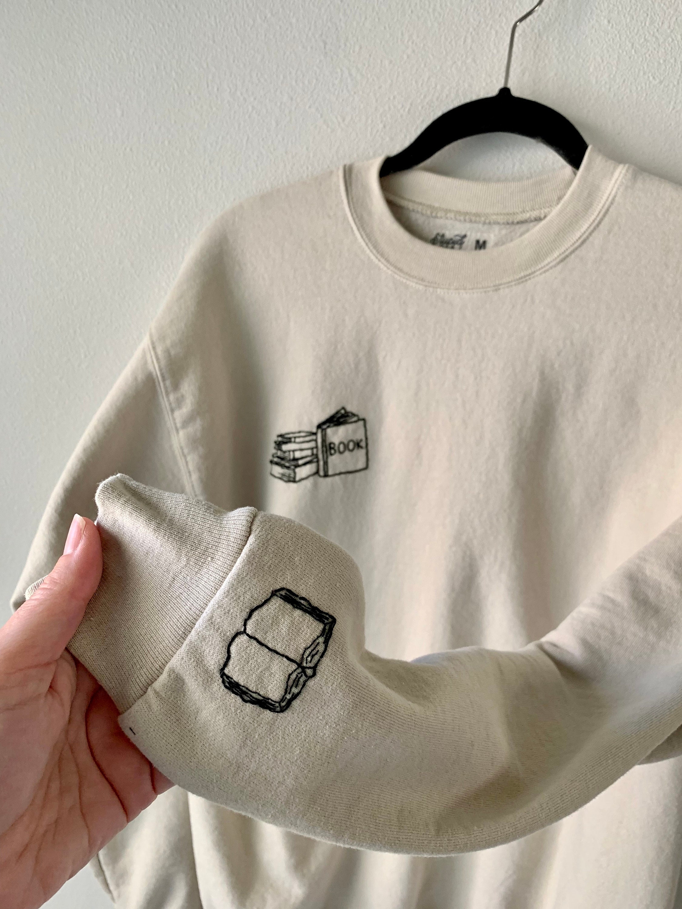 Book Lover’s Hand Embroidered Book Stack with Open Book on Sleeve, Tan Crewneck Fleece Long Sleeve Pullover Sweatshirt, Unisex, Bookstagram
