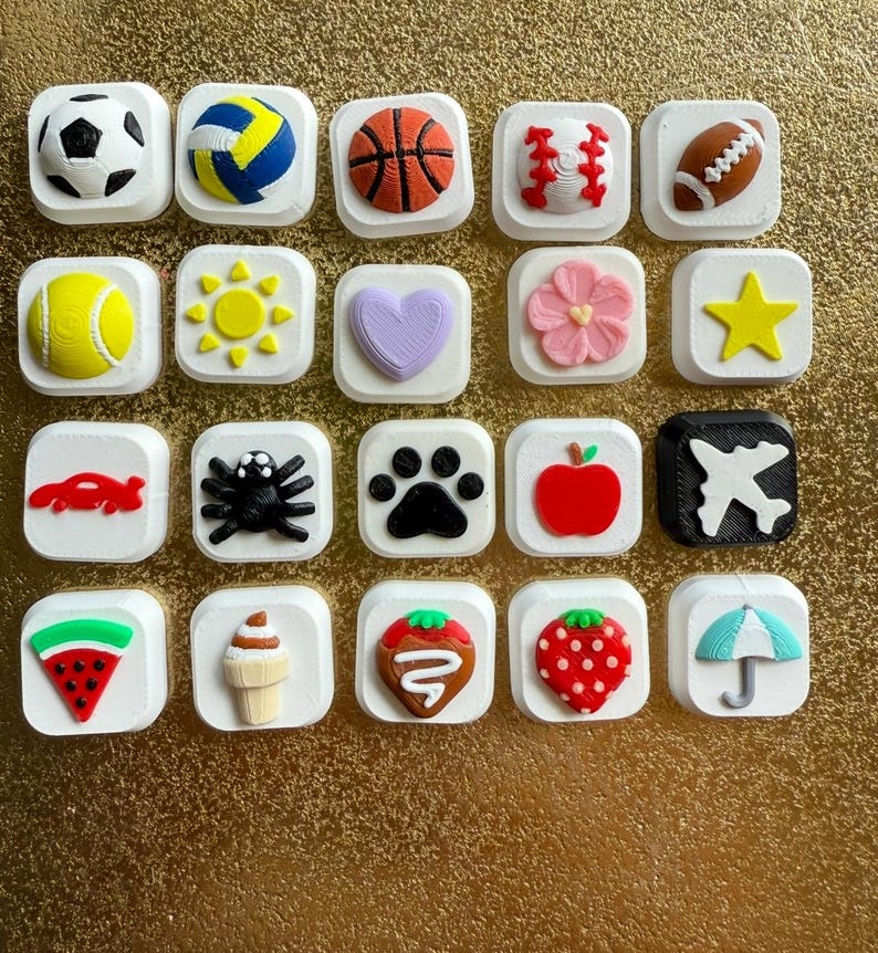 May include: A collection of twenty square white tiles, each featuring a distinct raised icon. The icons include various sports balls, a sun, a heart, a flower, a star, a car, a spider, a paw print, an apple, an airplane, a watermelon slice, an ice cream cone, strawberries, and an umbrella.