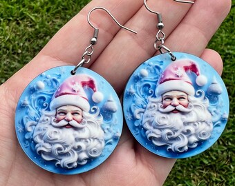 May include: A pair of blue and white Christmas earrings featuring a Santa Claus design. The earrings are made of wood and have silver hooks.