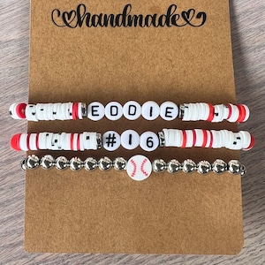 May include: Three bracelets with white and red beads, a baseball charm, and the name "EDDIE #16" spelled out in black letters.