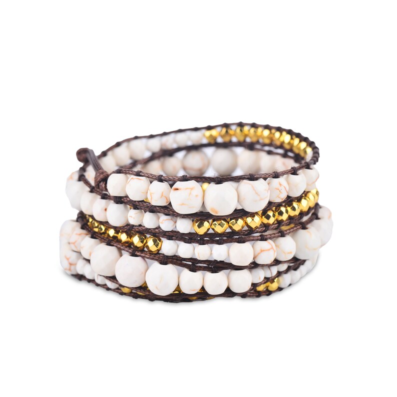 May include: A multi-strand bracelet with white and gold beads wrapped around brown cord.