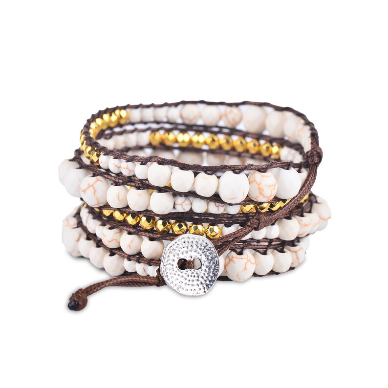 May include: A multi-strand bracelet with white beads, gold beads, and brown cord. The bracelet has a silver button closure.