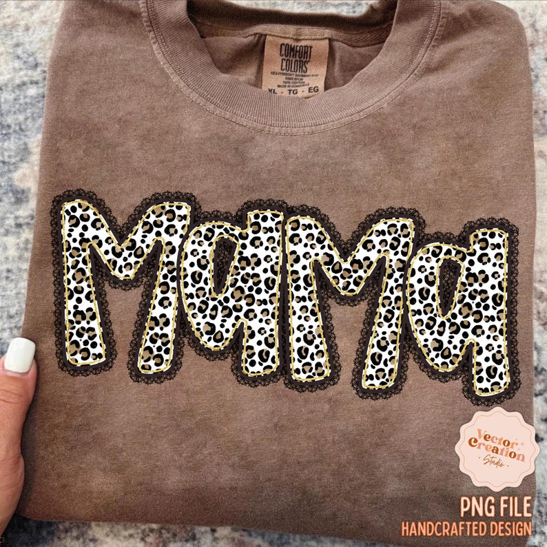 May include: Brown t-shirt with the word "Mama" in a leopard print design, outlined in gold and black lace. The shirt has a tag that says "Comfort Colors". The bottom right corner has a logo that says "PNG File Handcrafted Design".