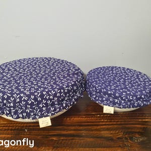 May include: Two round bowl covers made of dark blue fabric with a white dragonfly pattern. Each cover features an elasticized edge for a snug fit and a small rectangular beige fabric tag with the text "Aura Living" attached to the side.