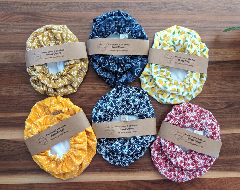 May include: Six reusable bowl covers with elastic edges, each wrapped in a brown paper band labeled Waterproof & BPA free Bowl Cover no more plastic wrap. The covers feature various patterns including yellow flowers, blue floral, yellow lemons, yellow dots, blue geometric, and red geometric prints.