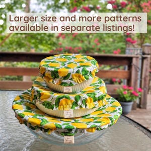 May include: Three round glass bowls stacked vertically, each covered with a fabric bowl cover featuring a yellow lemon and green leaf pattern. Each cover has a small rectangular tag. Text reads: Larger size and more patterns available in separate listings!