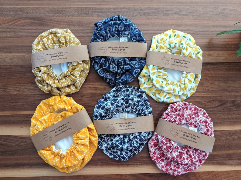 May include: Six reusable bowl covers in various patterns, including yellow with white flowers, blue with white flowers, white with yellow lemons, and red with white flowers. Each cover has a brown label that reads "Waterproof & BPA free Bowl Cover No more plastic wrap".
