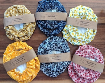 May include: Six circular fabric bowl covers with elastic edges, each wrapped in a paper band labeled 'Susu Living Waterproof & BPA free Bowl Cover no more plastic wrap'. The patterns include yellow daisies, blue floral, yellow lemons, yellow polka dots, blue geometric, and red starburst designs.