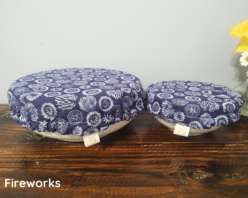 May include: Two round fabric bowl covers with an elasticized edge, featuring a dark blue background with a white repeating floral or firework-like pattern. Each cover has a small white rectangular tag labeled Sara Living attached to the side.