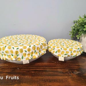 May include: Two round fabric bowl covers with an elasticized ruffled edge, featuring a white background with a repeating pattern of yellow yuzu fruits and green leaves. Each cover has a small rectangular fabric tag attached to the side.