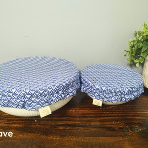 May include: Two round bowl covers featuring a blue and white wave pattern. Each cover has an elasticized edge and a small rectangular fabric tag. The covers are placed over white bowls, and the word Wave is printed in the bottom left corner.