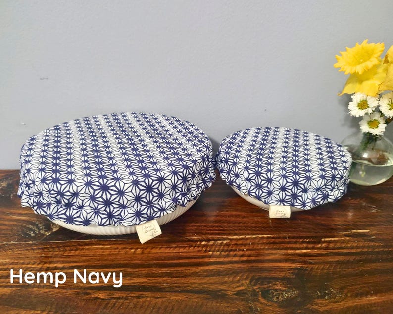 May include: Two round fabric bowl covers with an elasticized edge, featuring a navy blue and white geometric star pattern. Each cover has a small rectangular fabric tag attached to the side. The covers are placed over white ceramic bowls.