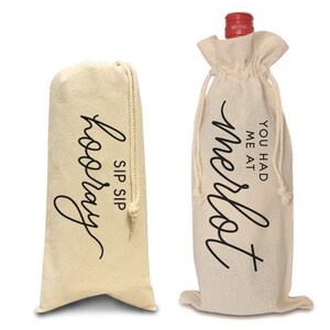 May include: Two white cotton wine bottle bags with black text. The bag on the left says "Sip Sip Hooray". The bag on the right says "You had me at Merlot".