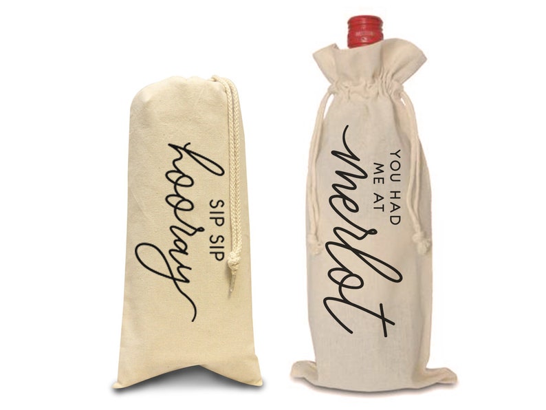 May include: Two white cotton wine bottle bags with black text. The bag on the left says "Sip Sip Hooray". The bag on the right says "You had me at Merlot".