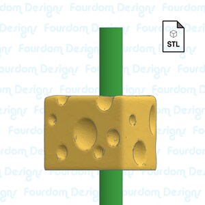 May include: A yellow, cube-shaped cheese block with several holes, pierced by a vertical green rod. The cheese has a slightly textured surface. A document icon with "STL" text is in the upper right corner.