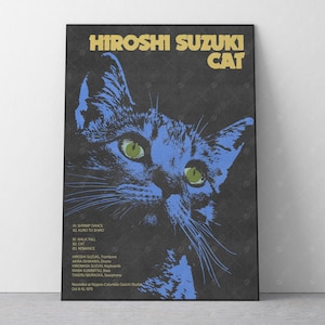 May include: A framed poster with a blue cat design and green eyes. The poster reads "HIROSHI SUZUKI CAT" in gold. Below the cat image are song titles and credits. The poster is on a grey textured background.