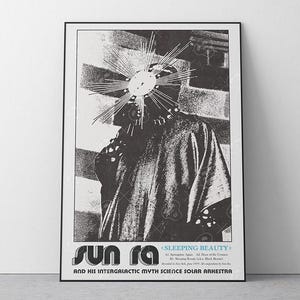 May include: Black and white poster featuring Sun Ra, with a sunburst headpiece. The poster includes the text "SUN RA" in stylized lettering, and the title "SLEEPING BEAUTY". The poster is framed in a black frame.