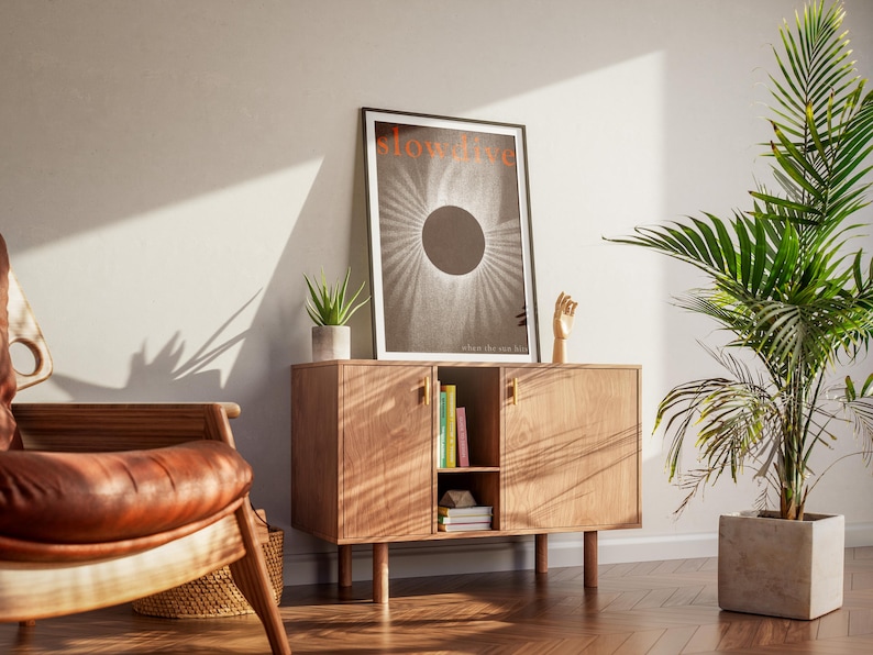 Puede incluir: Un mueble de madera con un p&oacute;ster enmarcado que dice "slow fire" y un gr&aacute;fico en blanco y negro. Una peque&ntilde;a planta en maceta y una escultura de mano de madera est&aacute;n encima. Una silla de cuero y una planta grande en maceta tambi&eacute;n est&aacute;n en la habitaci&oacute;n.