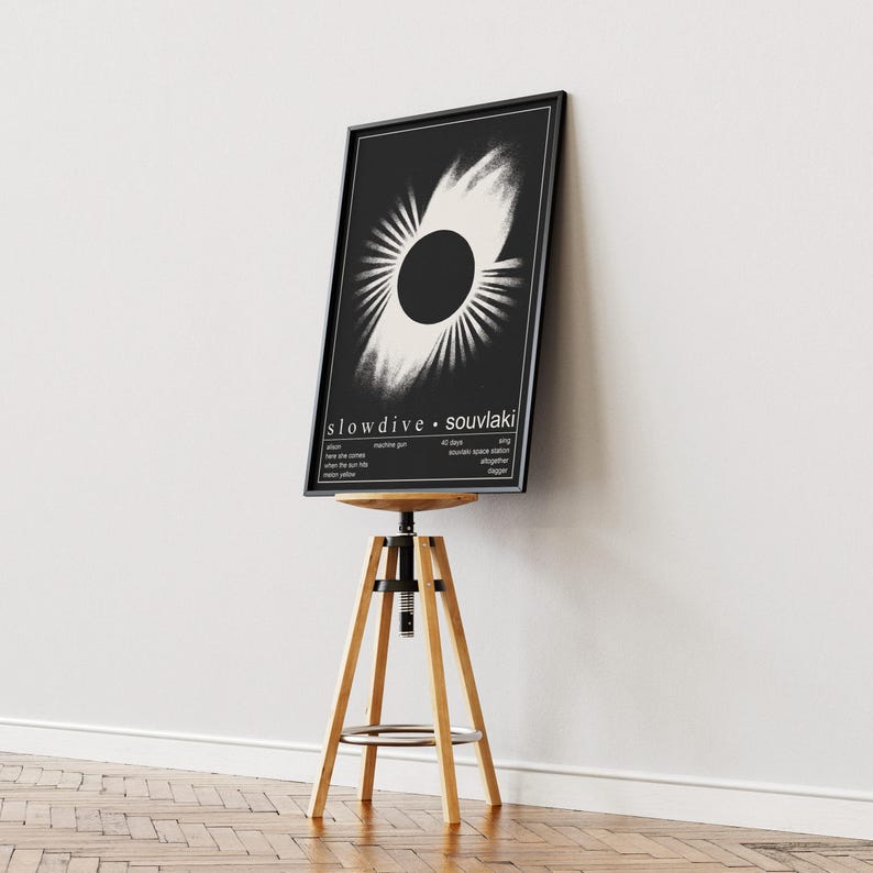 May include: A framed black and white poster with a circular design and the text "slowdive &bull; souvlaki." The poster is displayed on a wooden stool with a black seat. The background is a white wall and a wooden floor. The stool is approximately 76 cm tall.